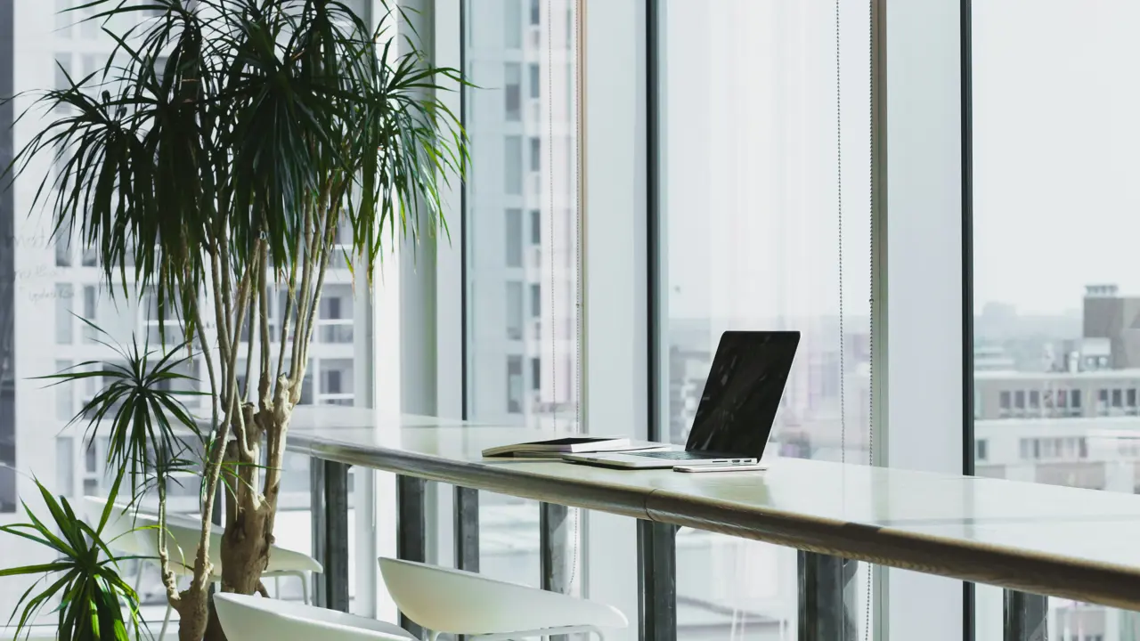 Tibco Services modern workspace in a skyscraper with a table beside a large window, featuring a computer and a view of the city skyline.